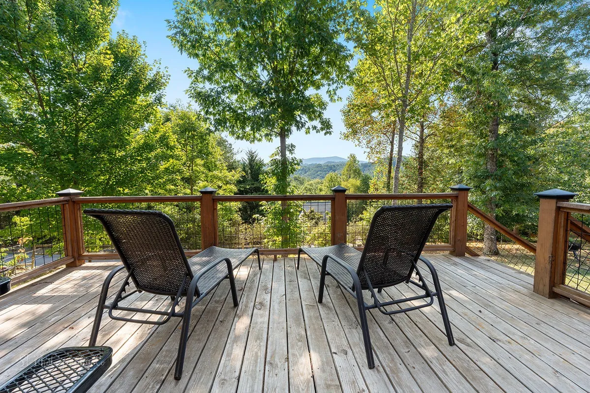 A tranquil outdoor deck with comfortable chairs, wooden railing, and sweeping mountain views framed by trees. This peaceful setting highlights the scenic beauty accessible from the cabin itself.
