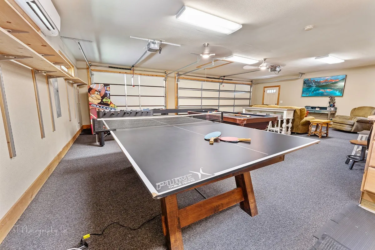 A dynamic game loft setting with a ping pong table, comfortable seating area, and game consoles. The arrangement fosters both energetic play and relaxed socializing, with the seating and TV establishing the secondary lounge vibe.