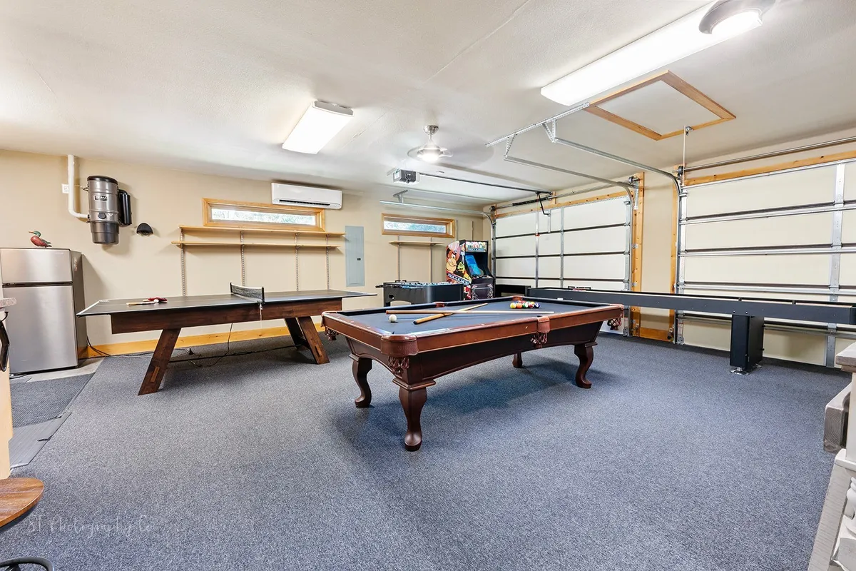 This image captures a vibrant game room featuring a pool table, ping pong table, an arcade machine, and a refrigerator. The space looks bright and energetic, with plenty of room for multiple players to enjoy different games simultaneously. The mini fridge visible in the corner emphasizes convenience for snacks and drinks during play.