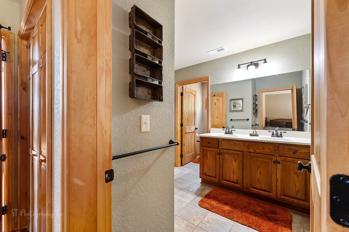 A well-appointed bathroom featuring a double vanity with sinks, wooden cabinetry, a large mirror, and a cozy rug. The space feels inviting and functional, ideal for daily routines and self-care. The overall mood is serene and welcoming, making it a pleasant spot to start or end the day.