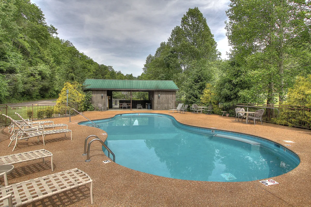 A sparkling community swimming pool is surrounded by verdant greenery, with poolside lounge chairs and a covered gazebo offering a relaxing, family-friendly space for cooling off and socializing. The atmosphere is calm and inviting, ideal for groups of all ages.