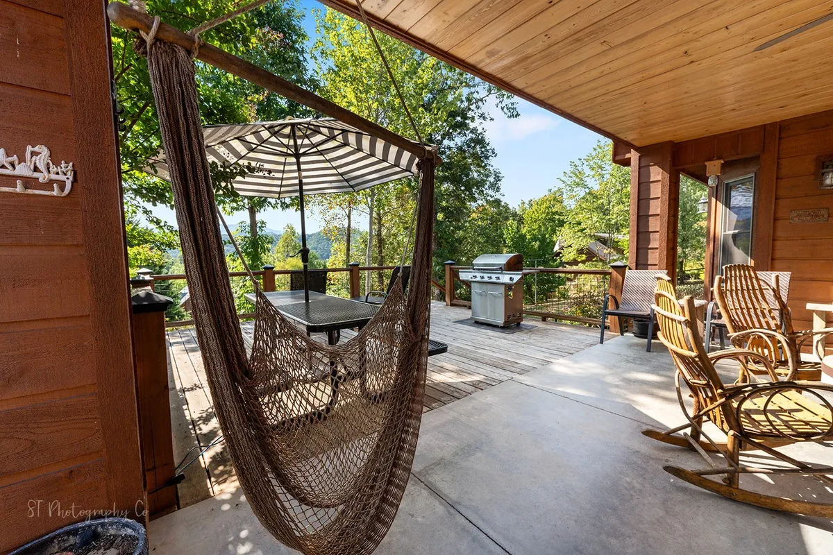 A spacious deck with rocking chairs, hammock, grill, dining table, and canopy, surrounded by peaceful woodlands. The inviting setting encourages relaxation and enjoying nature together.