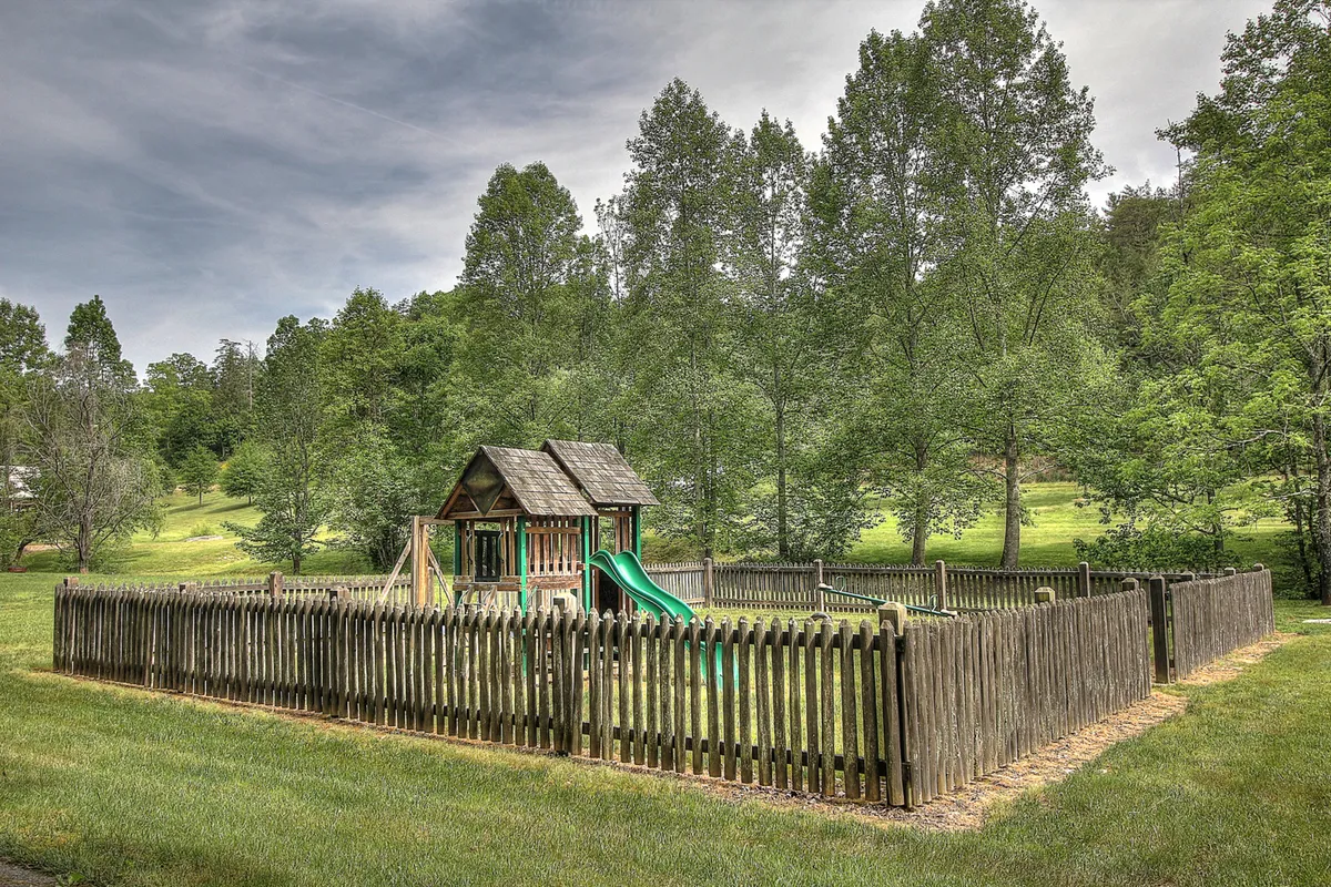 A vibrant playground surrounded by a wooden fence and lush greenery, filled with children playing and families gathering, evoking joyful energy and a welcoming atmosphere.