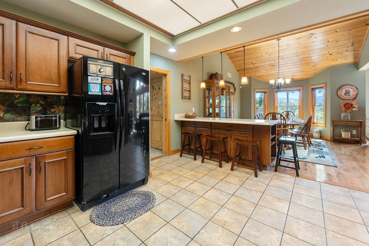 This image features a warm, homey kitchen with wooden cabinetry, a black refrigerator, a dining table with chairs, and a breakfast bar. The design encourages social cooking and casual dining, supporting group activities and conversation.