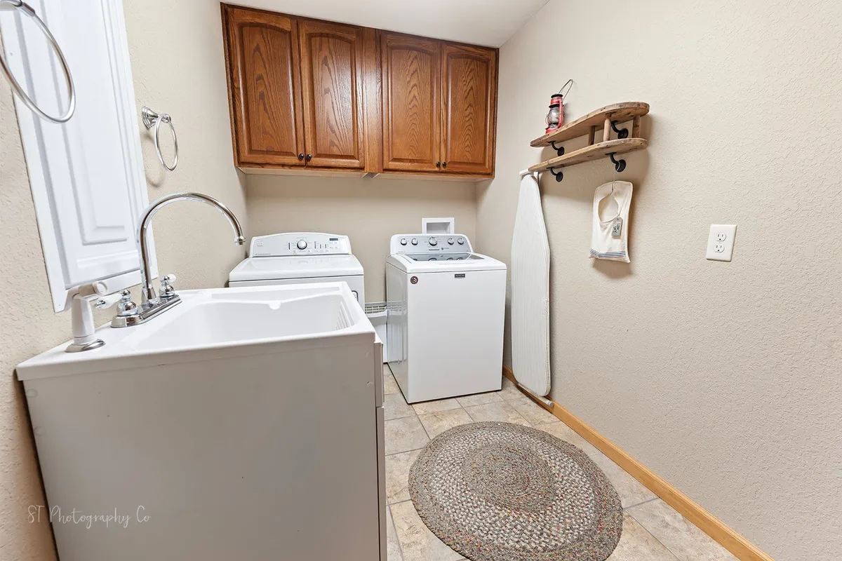 A tidy, functional laundry room is shown with a washing machine, dryer, sink, ironing board, and organized wooden shelving for supplies. The space is practical yet inviting, ready to support long stays and all-weather adventures.