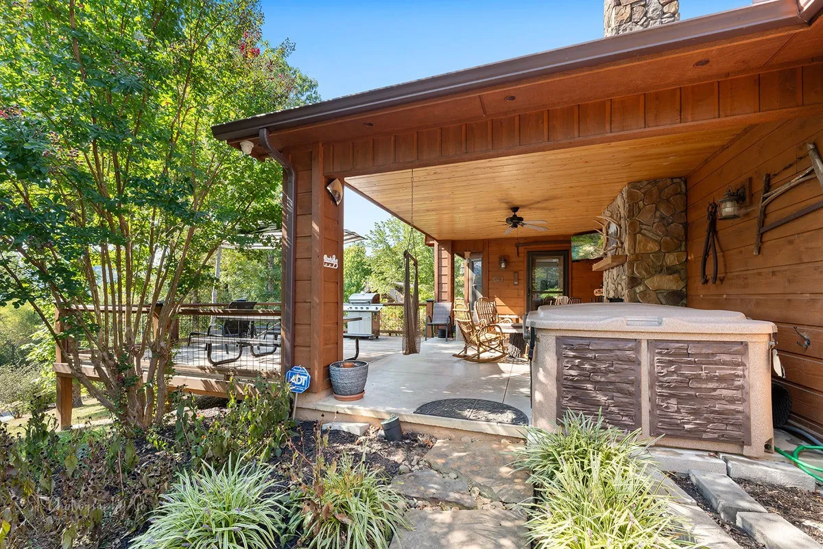 An outdoor area featuring a hot tub, seating, a stone wall, and a grill, all set against a backdrop of trees. The space is designed for relaxation, outdoor dining, and gatherings—ideal for unwinding after a day out exploring Pigeon Forge.